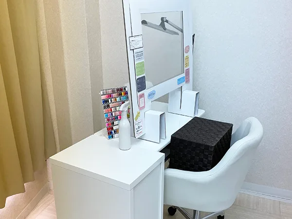 無人の施術ブースを引きで見たところ。白いデスクとキャスターチェア、ベージュのカーテン